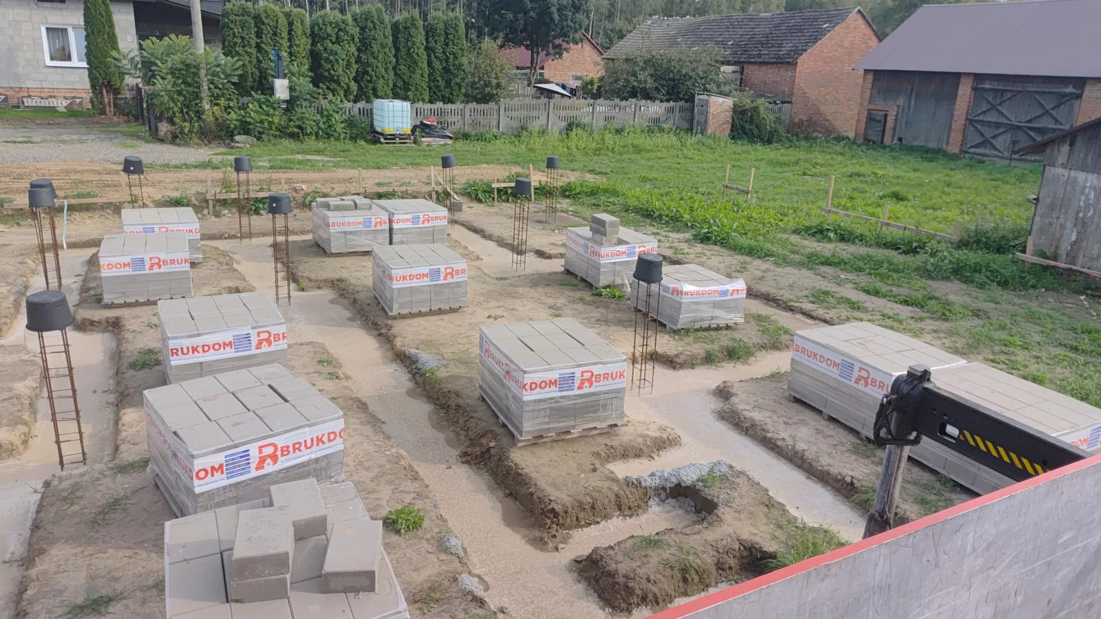 Palety bloczków fundamentowych Brukdom rozłożone wzdłuż ław fundamentowych domu